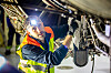 Aircraft technician wearing a high-visibility vest inspects equipment beneath an aircraft.