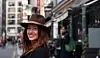 Linda Iliste smiling in a brown hat and dark coat on a city street.